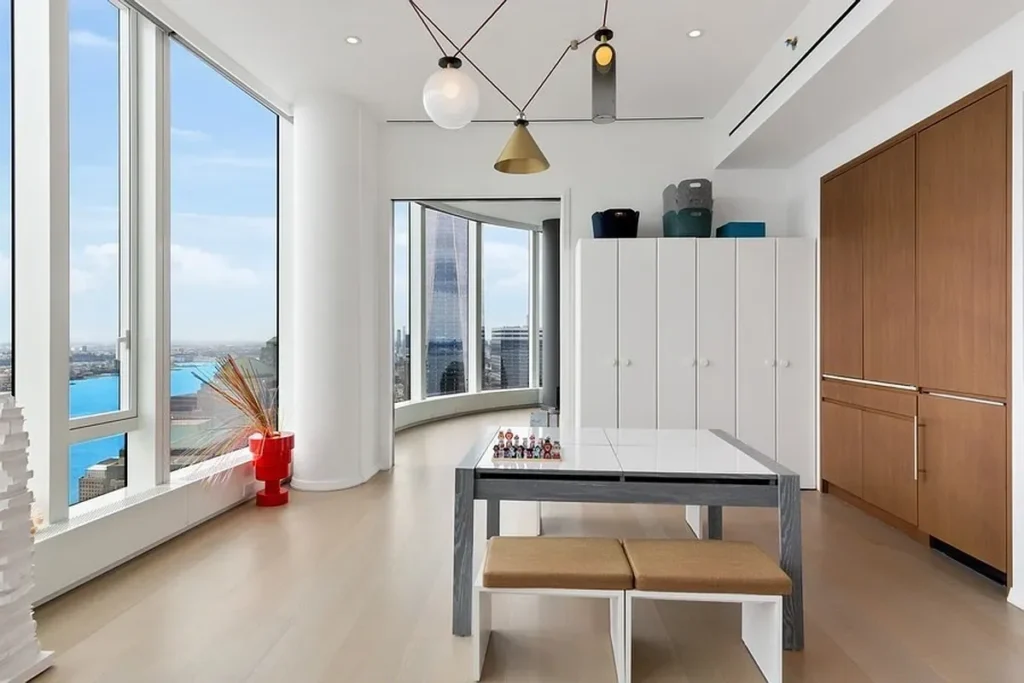 A room with a table and chairs, a bench, and a large window.