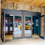 A building with two doors open and a taxi in the background.