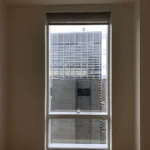 A window with blinds in the corner of an empty room.