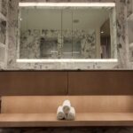Elegant spa room with a large mirror, soft lighting, and rolled towels on a bench.