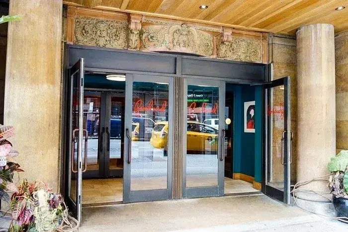 A building with two doors open and a taxi in the background.